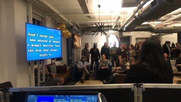 Colleagues at a karaoke team building event with lyrics on the screen